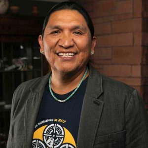 Dr. Darold Joseph wearing an NAU t-shirt, dress coat, and turquoise necklace