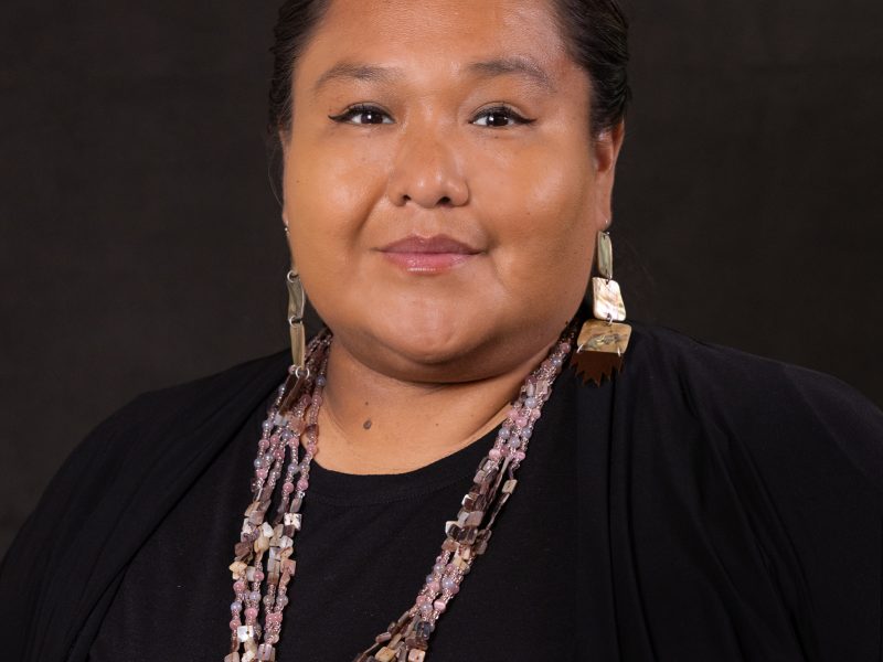 Sanjiv Thompson wearing a black top, pink beaded necklace, and long shiny earrings