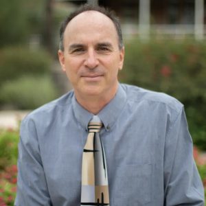 Photo of Chris Segrin in a grey button up and multicolored tie