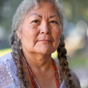 Joyce Tovar wearing a white topic and red coral necklace with her hair braided into two braids