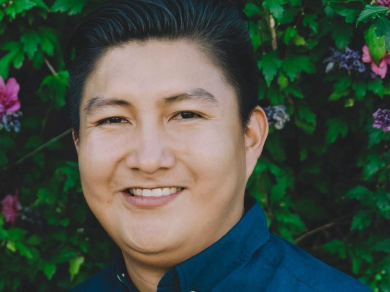 Michael Sam wearing a navy blue button up with a natural floral background