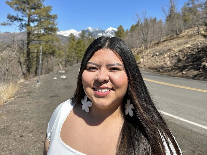 Sunflower Huskie wearing a white top and white flower earrings with nature in the background