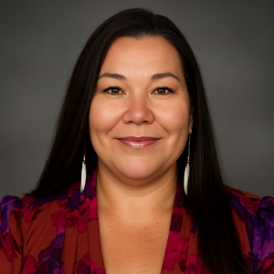 Headshot photo of Brandie Franco with a red and purple top and white dangly earrings with a gray background.