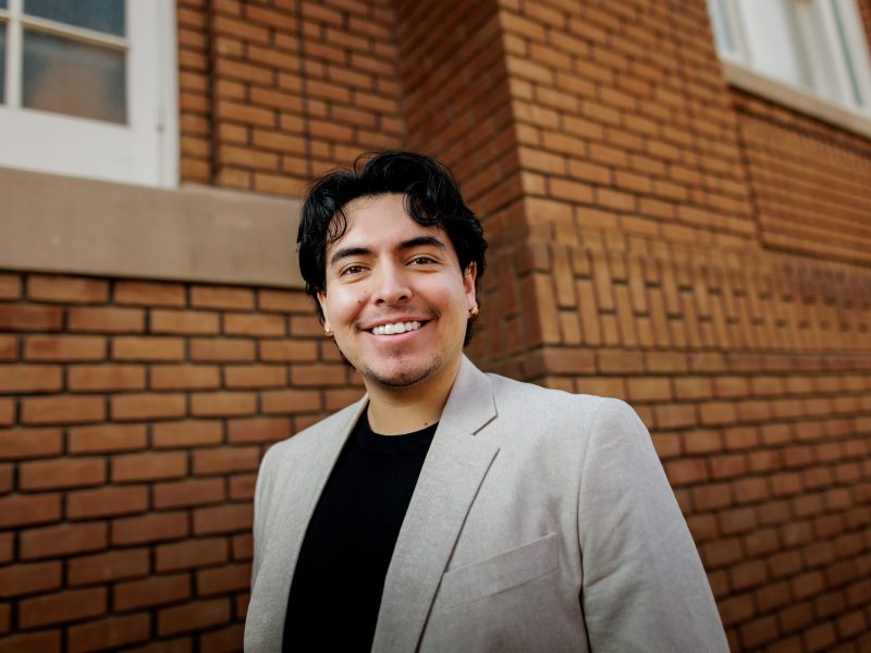 Headshot photo of Gabriel Baca wearing a black top and tan blazer with a brick background. Photo courtesy of Native Forward Scholars Fund.