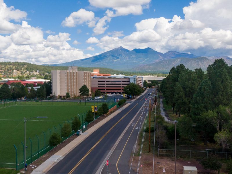 Drone shot showing road on campus, buildings, and the San Francisco Peaks.