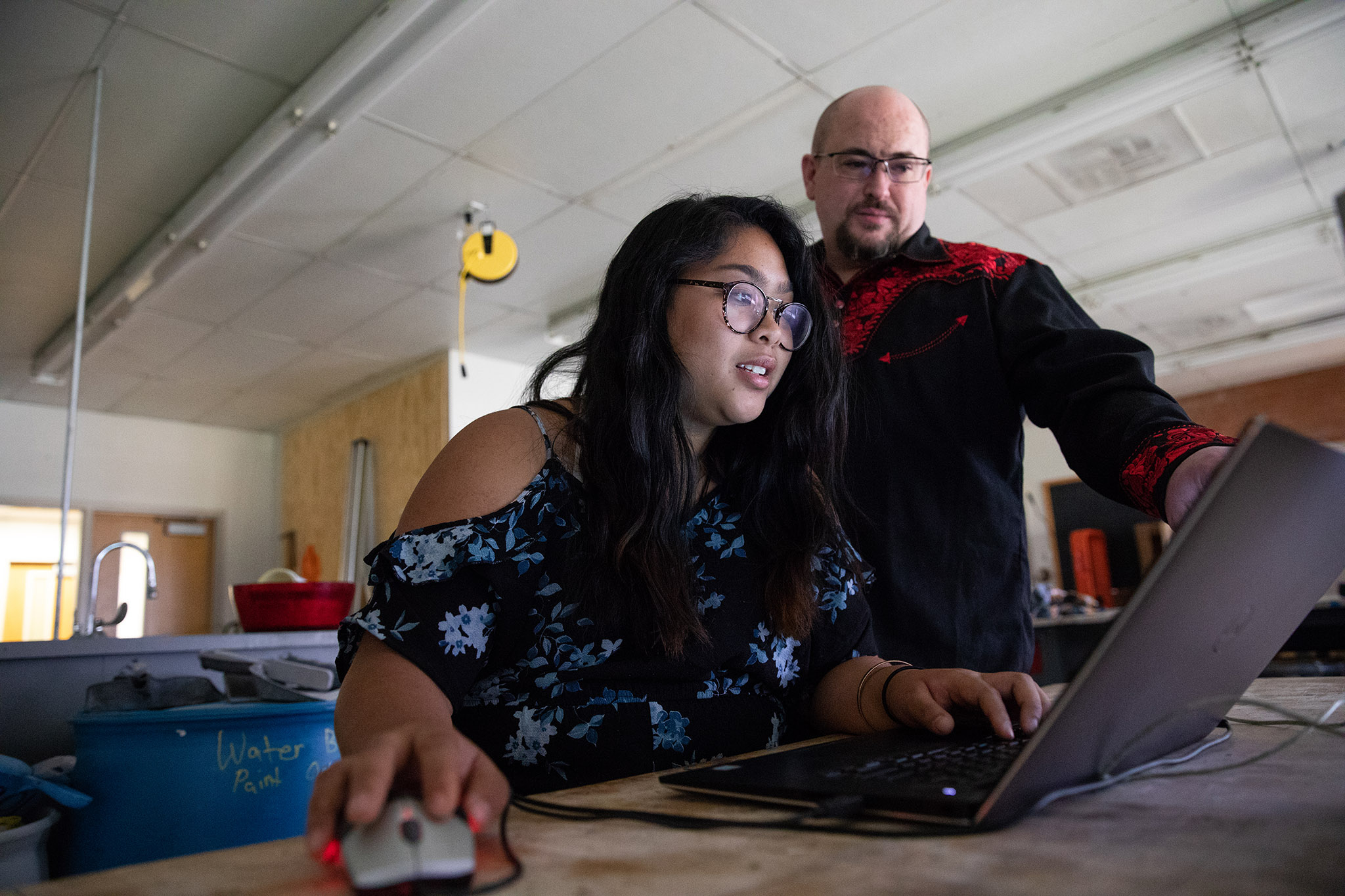 Student works on laptop while professor watches.
