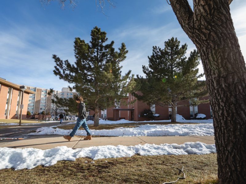 A student walking through a partly snowy campus.