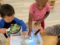 Two children looking at sand in a bin with a magnifying glass.