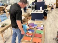 A child showing his mom and dad a homemade book he made out of drawings, folded into construction paper.