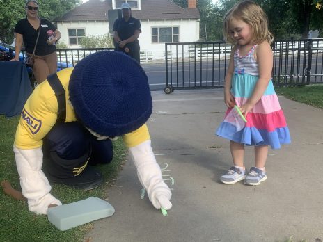 Louie the Lumberjack drawing with sidewalk chalk next to a girl smiling