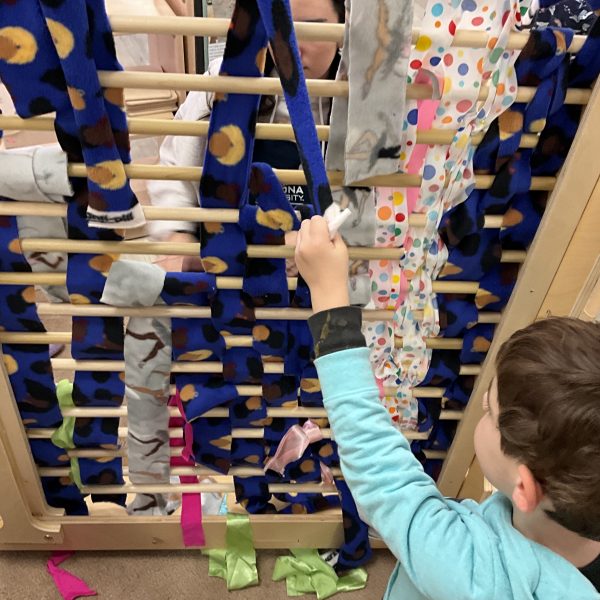 A child pulling on blue fabric in a classroom loom.