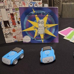 A table displaying two books about robots, with three small remote cars and colored platforms.