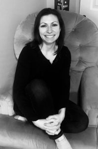 A black and white photo of a female wearing black, sitting cross legged in a rocking chair.