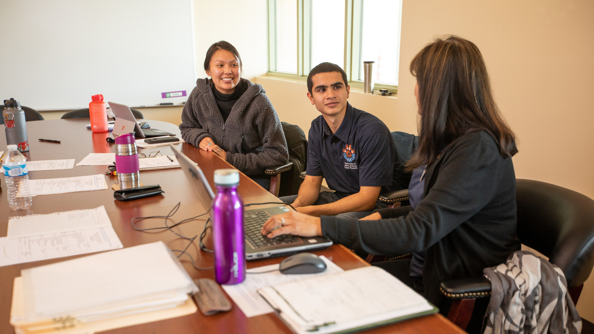 three native american adults talking in front of open laptops at a conference table