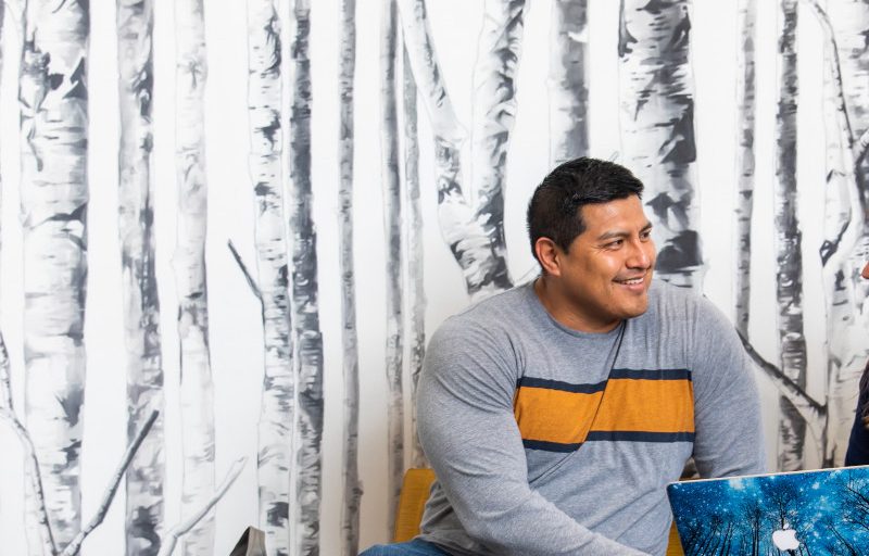 Northern Arizona University students talking in a hall decorated with aspen tree wallpaper.