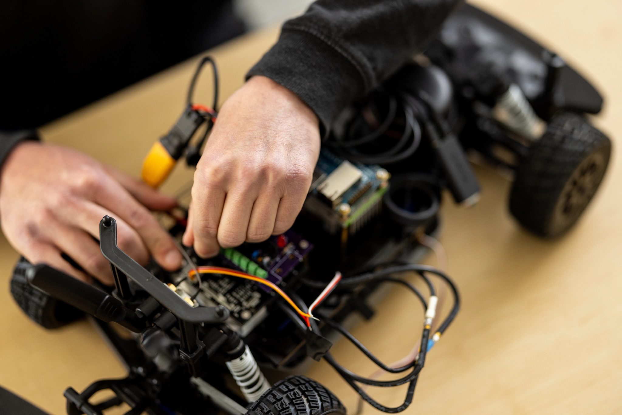 A pair of hands working on a remote-controlled car on a table.