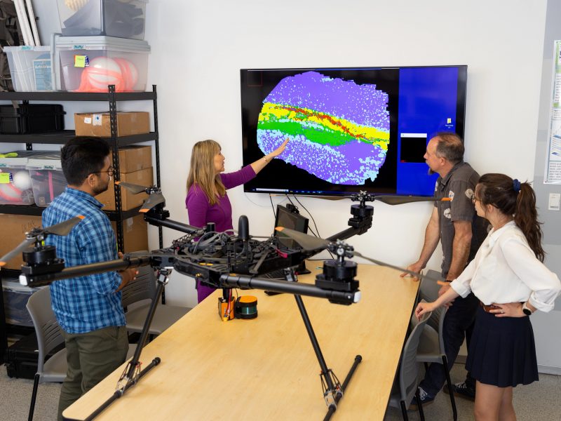Students and professors analyzing a thermal map taken by a large drone.