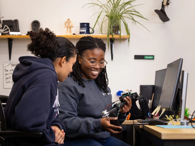 Two students working together on an electronic device and smiling.