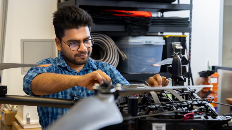 Student working on the wiring of a large drone on a table.