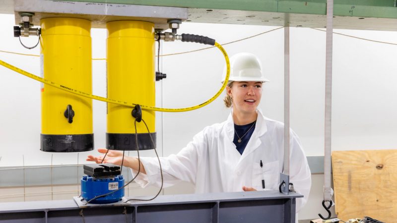 Student in white hard hat and lab coat working with a piece of equipment.