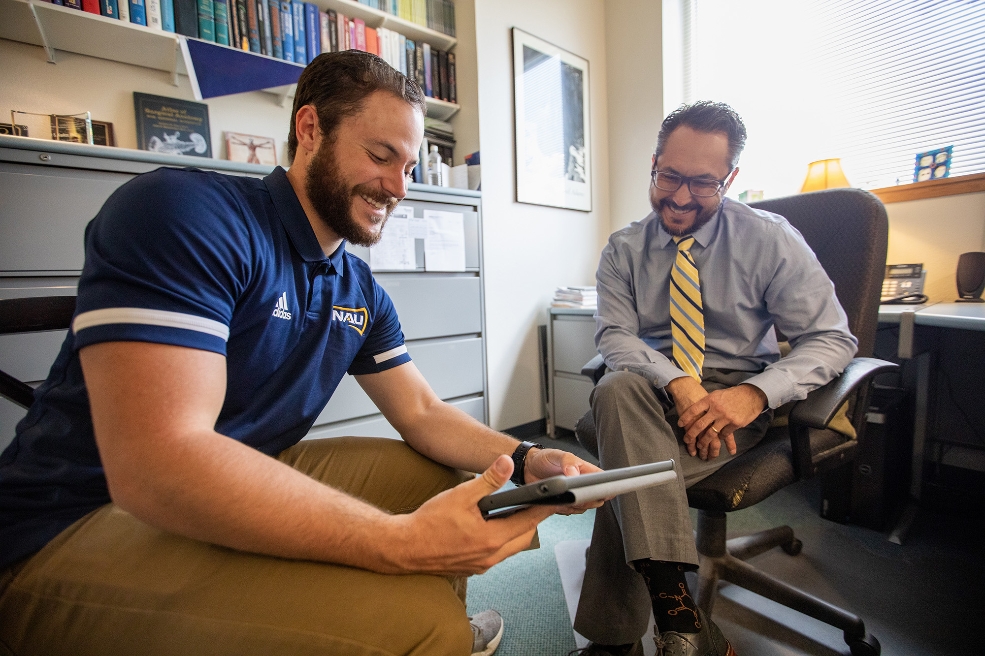 Mentor and his mentee talking and smiling while looking at an ipad.