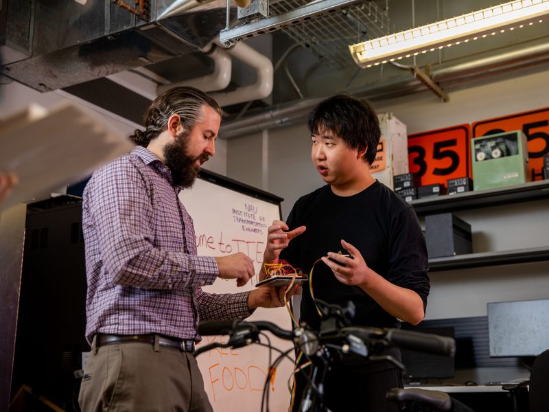 Two men working on a circuit board for a smart bike.