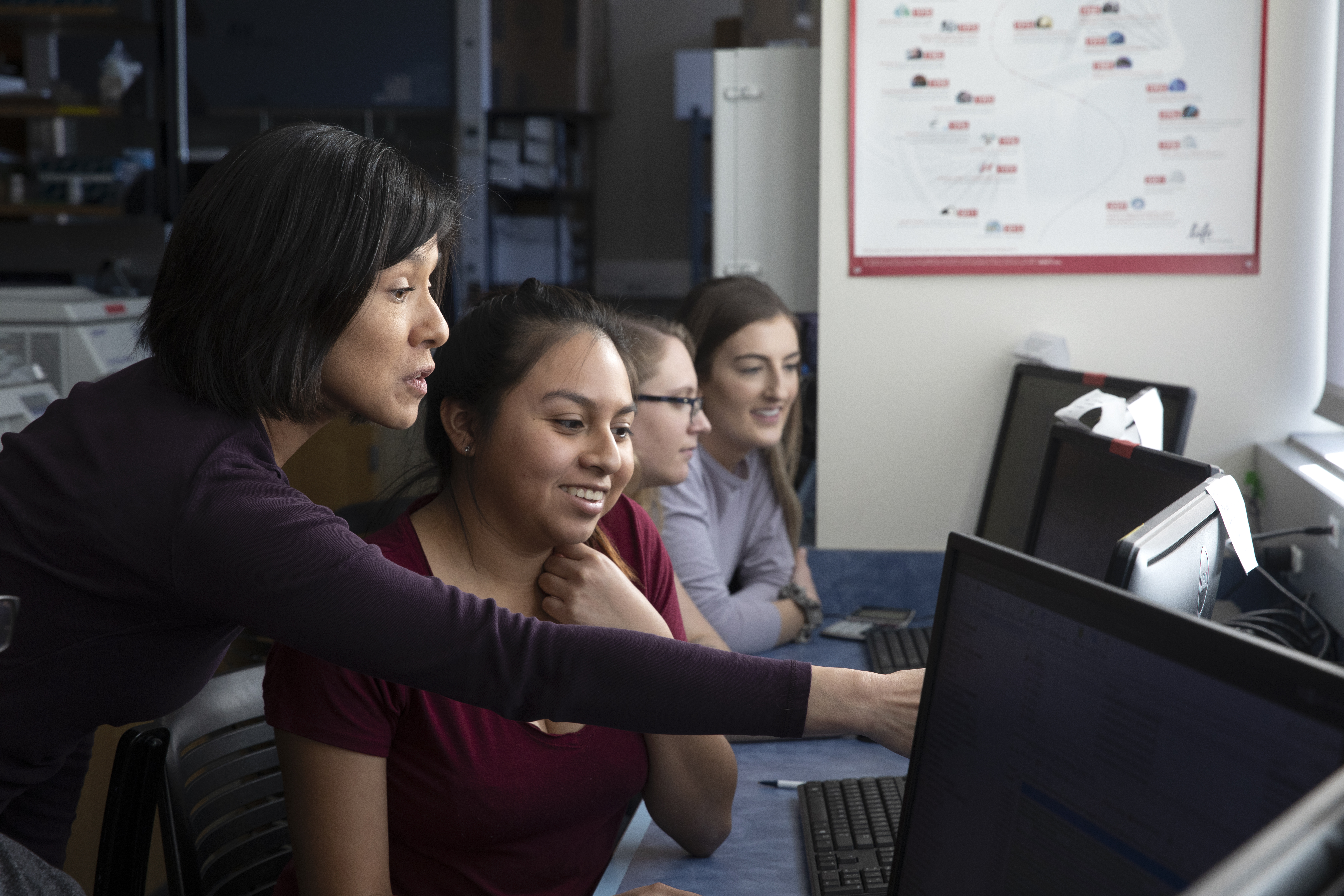 Professor helps student sitting at computer.