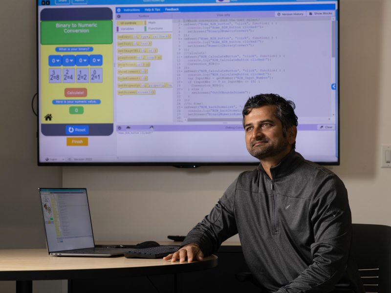 Ashish Amresh sits at table with laptop and screen protector behind him.