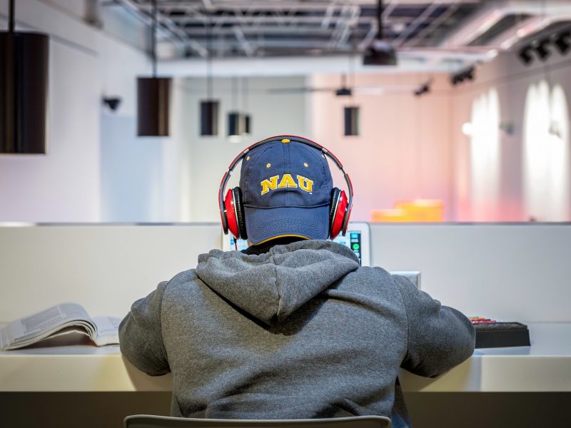 N A U student sitting at desk on a laptop with a backwards N A U hat.