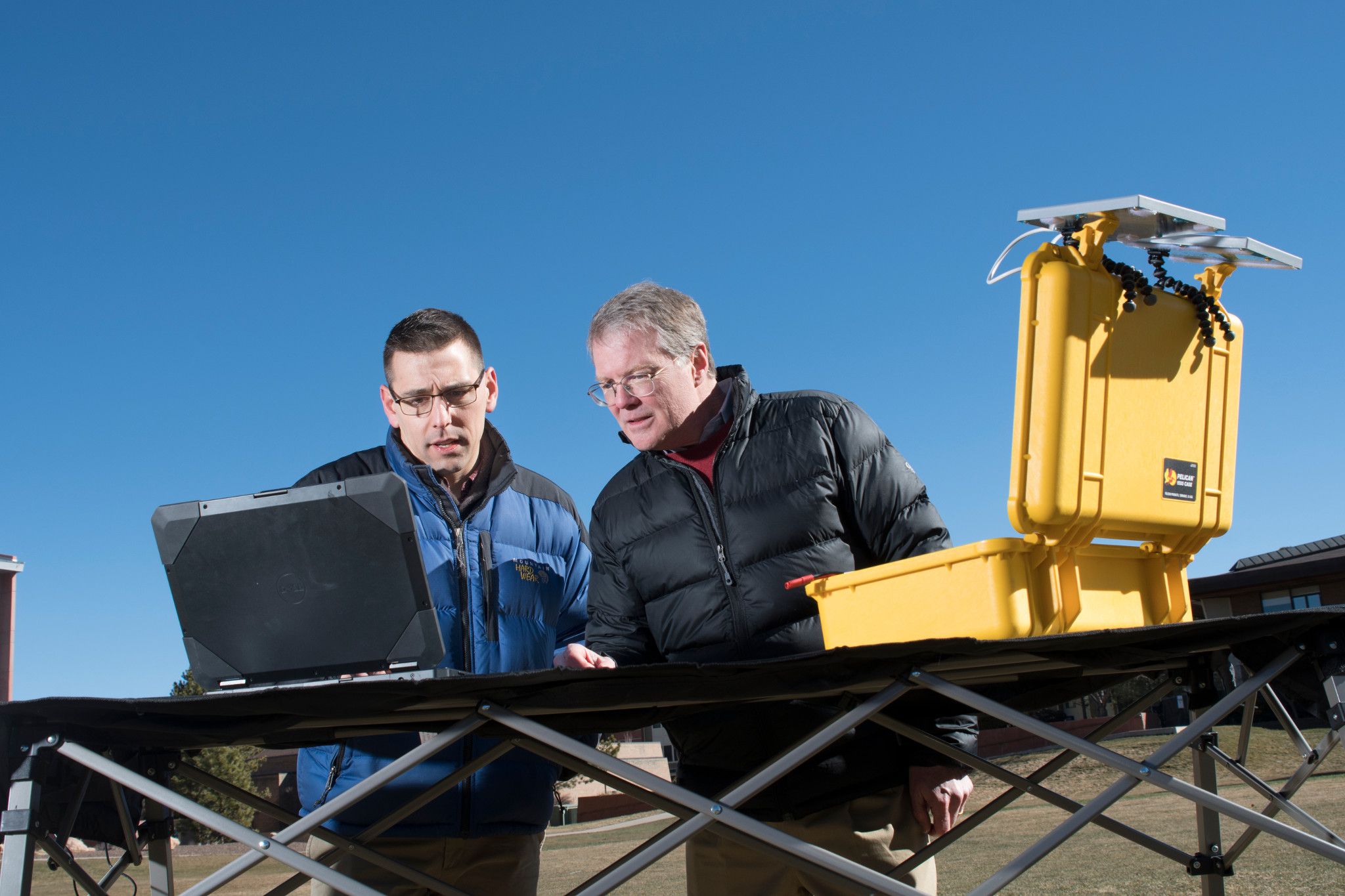 Two men working together on a laptop outside to program a drone.