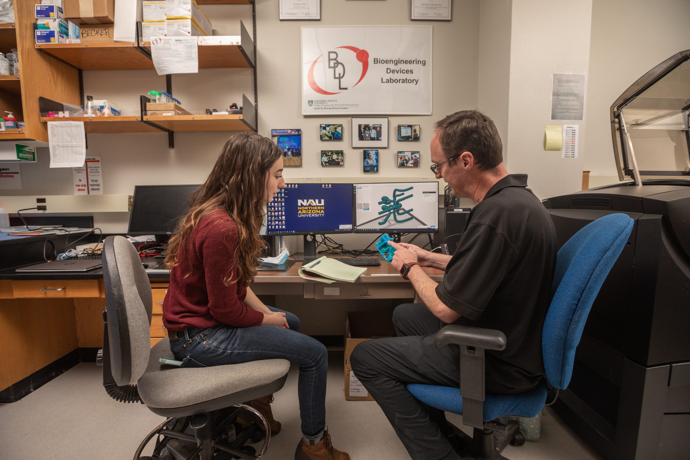 Student and professor are sitting at a desk and professor is explaining something to student.