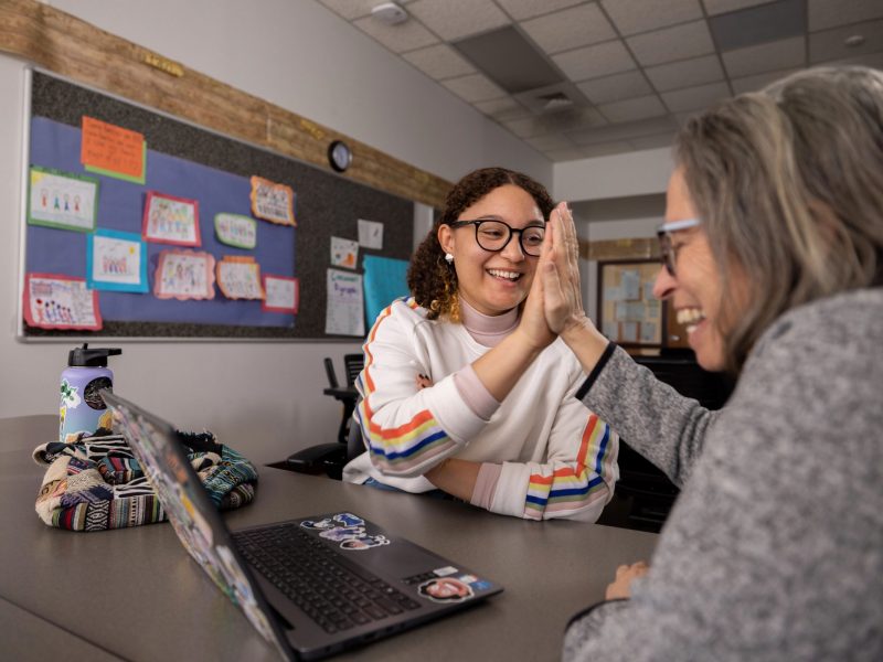Mentor and student are sitting in a classroom and giving each other a high five.