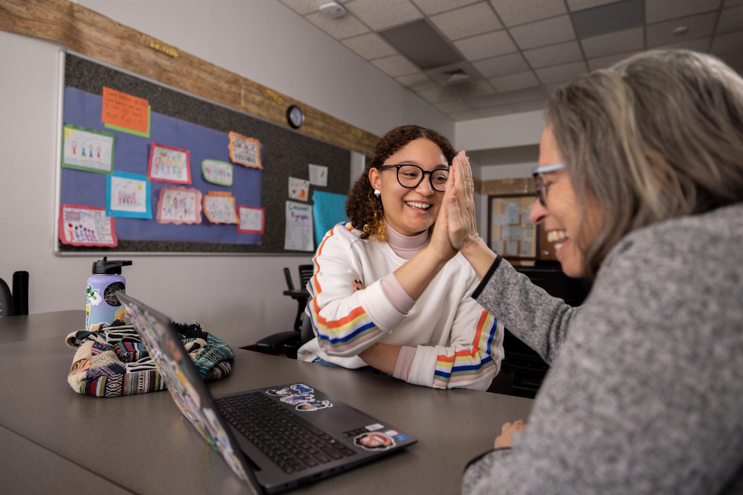 Mentor and student are sitting in a classroom and giving each other a high five.