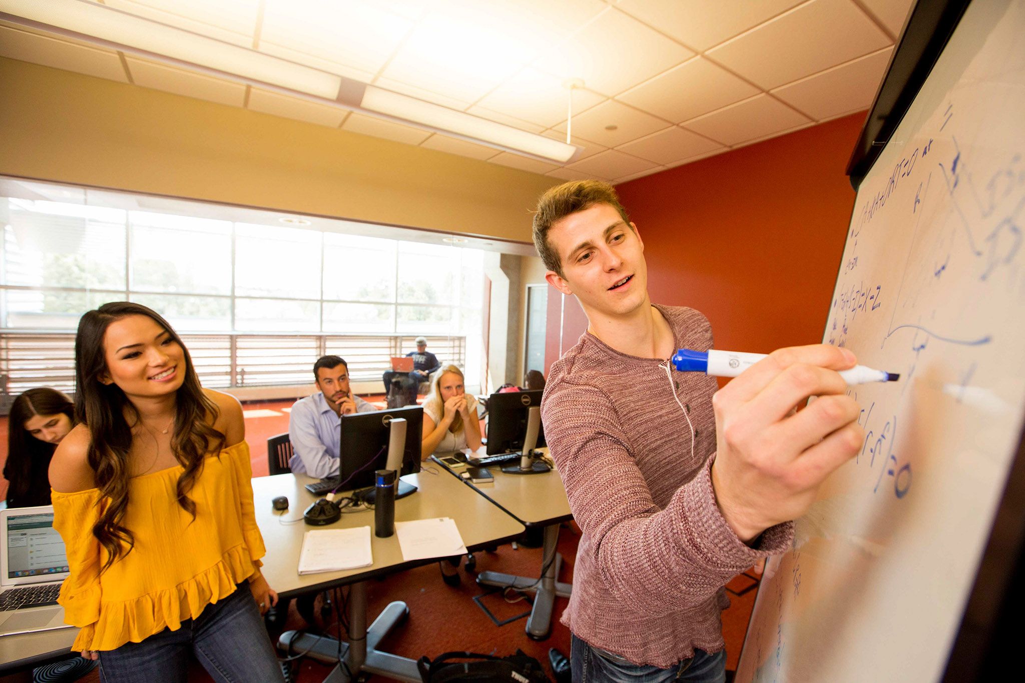 Peer Mentor helping students by solving math problems on whiteboard.