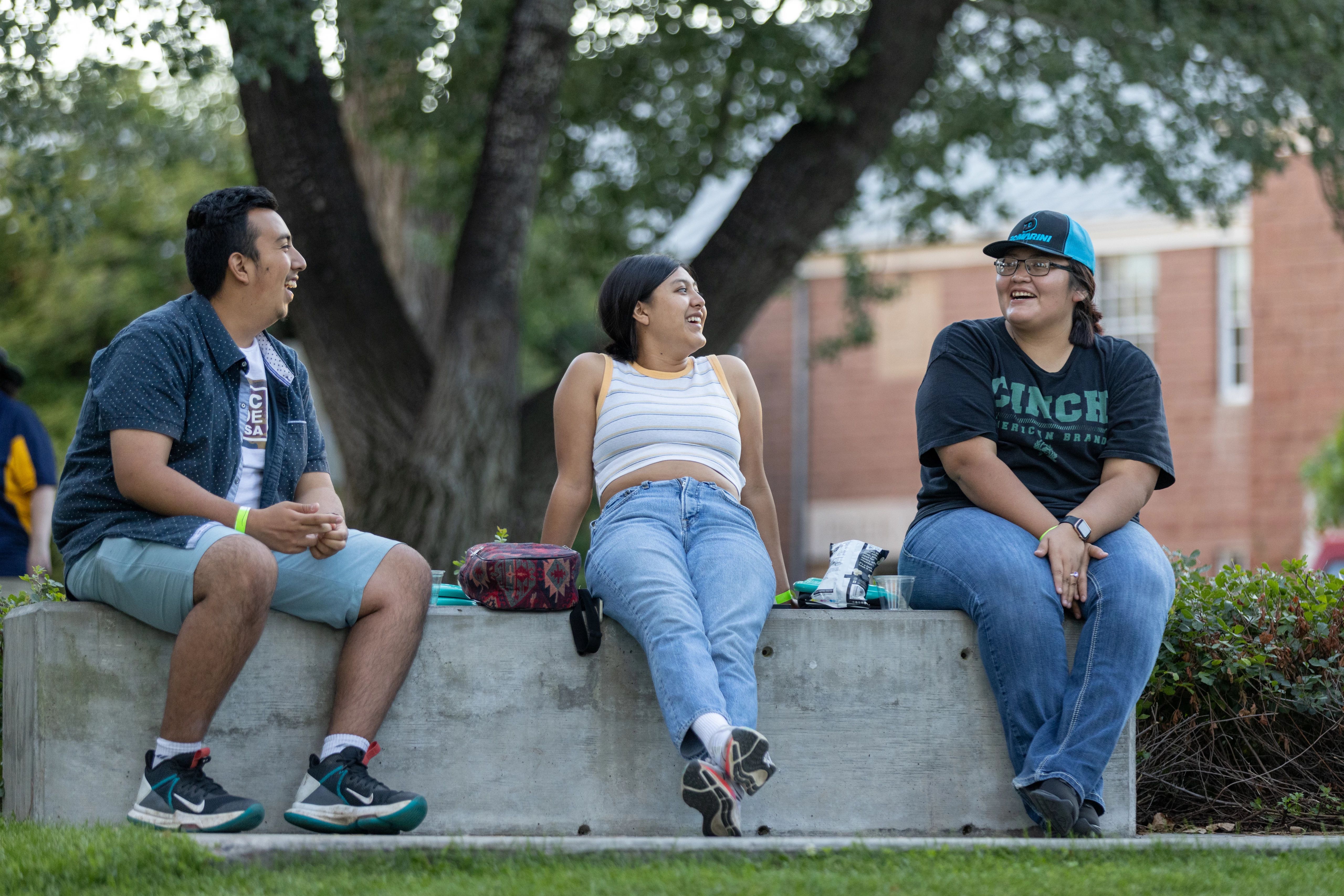 Three student are sitting together out and having a picnic.