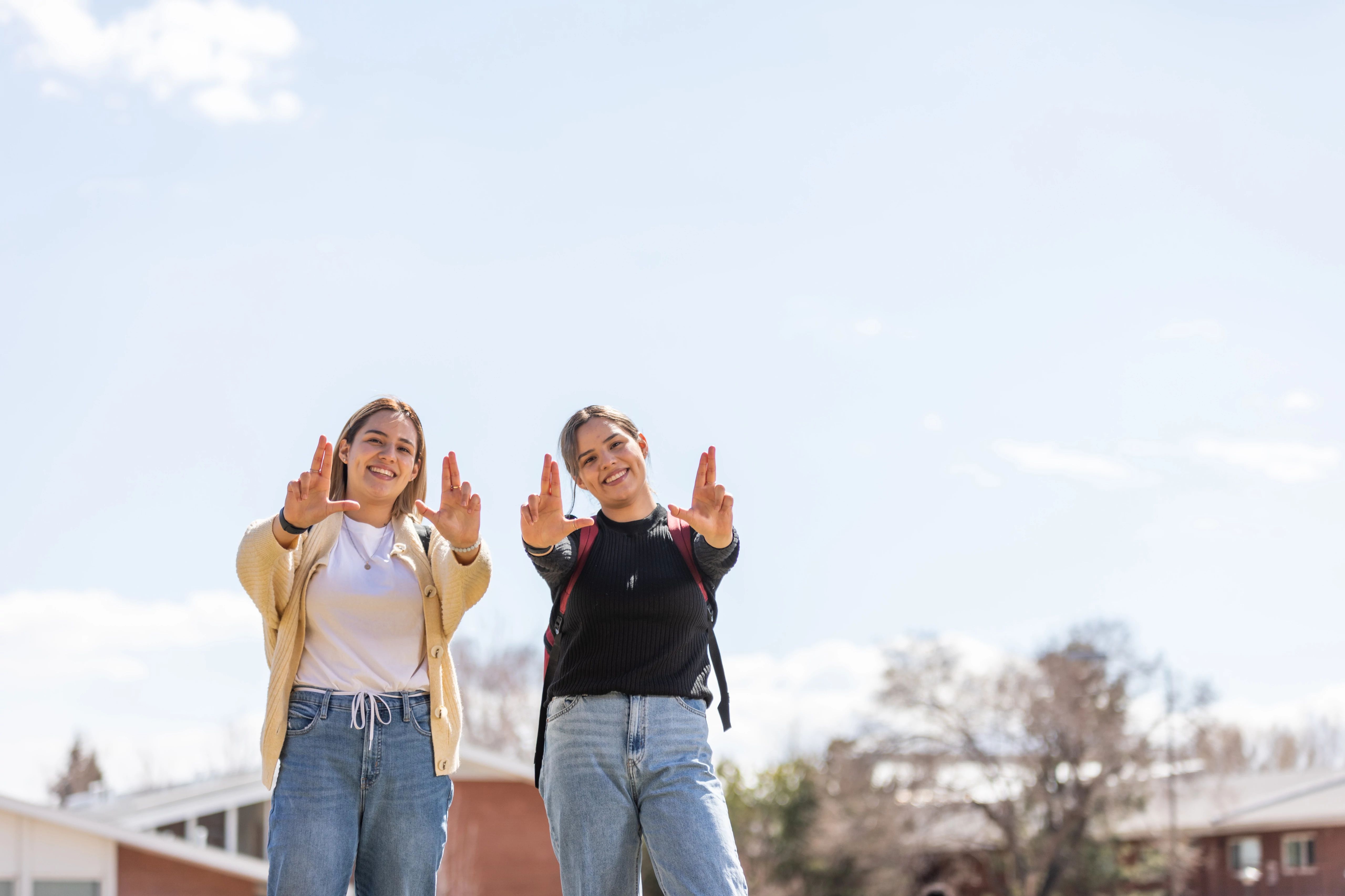 Two students who are both first-generation students making the iconic Lumber Jack hand pose on the N A U campus.