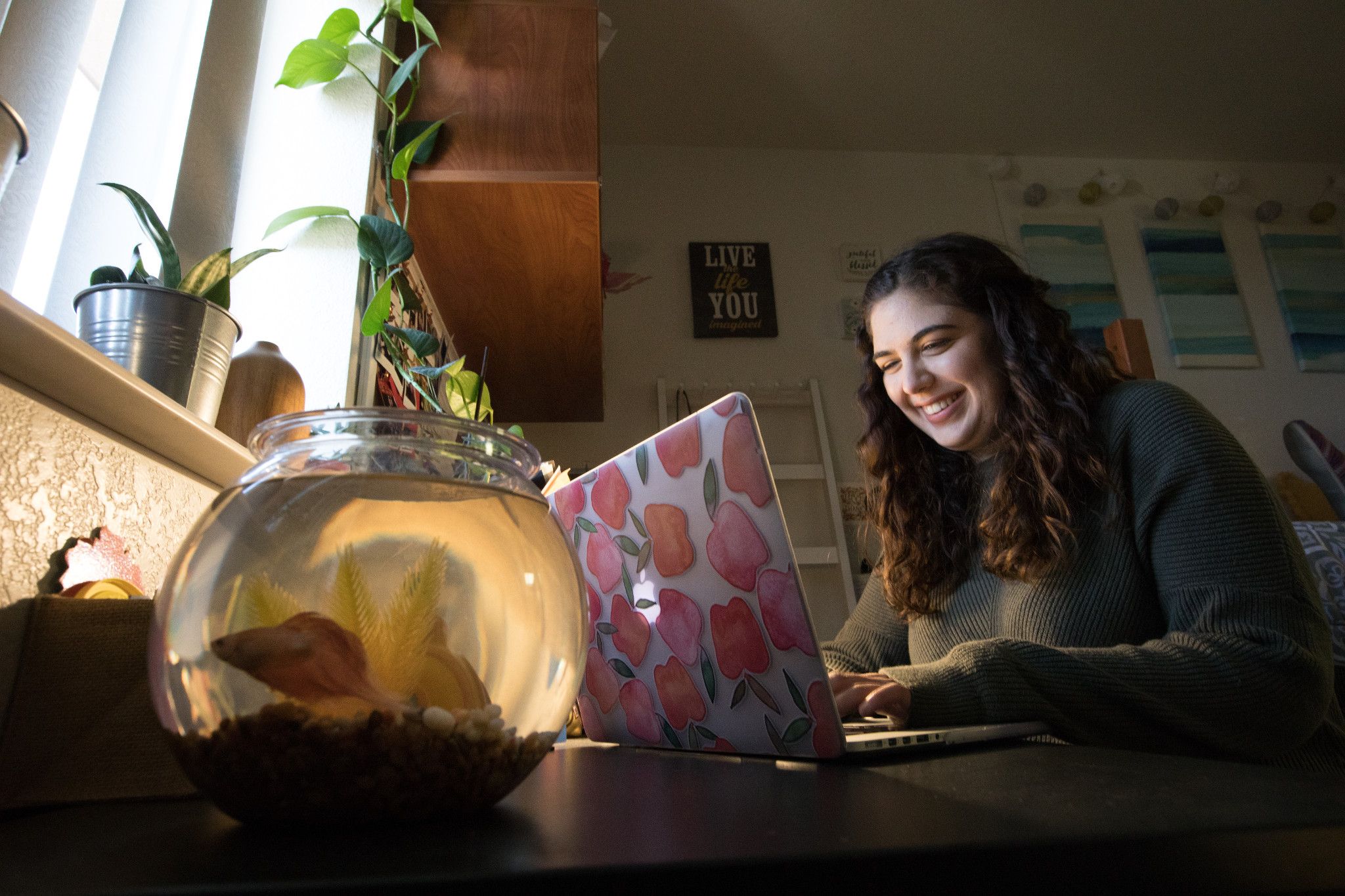 Student in dorm room smiling at computer.