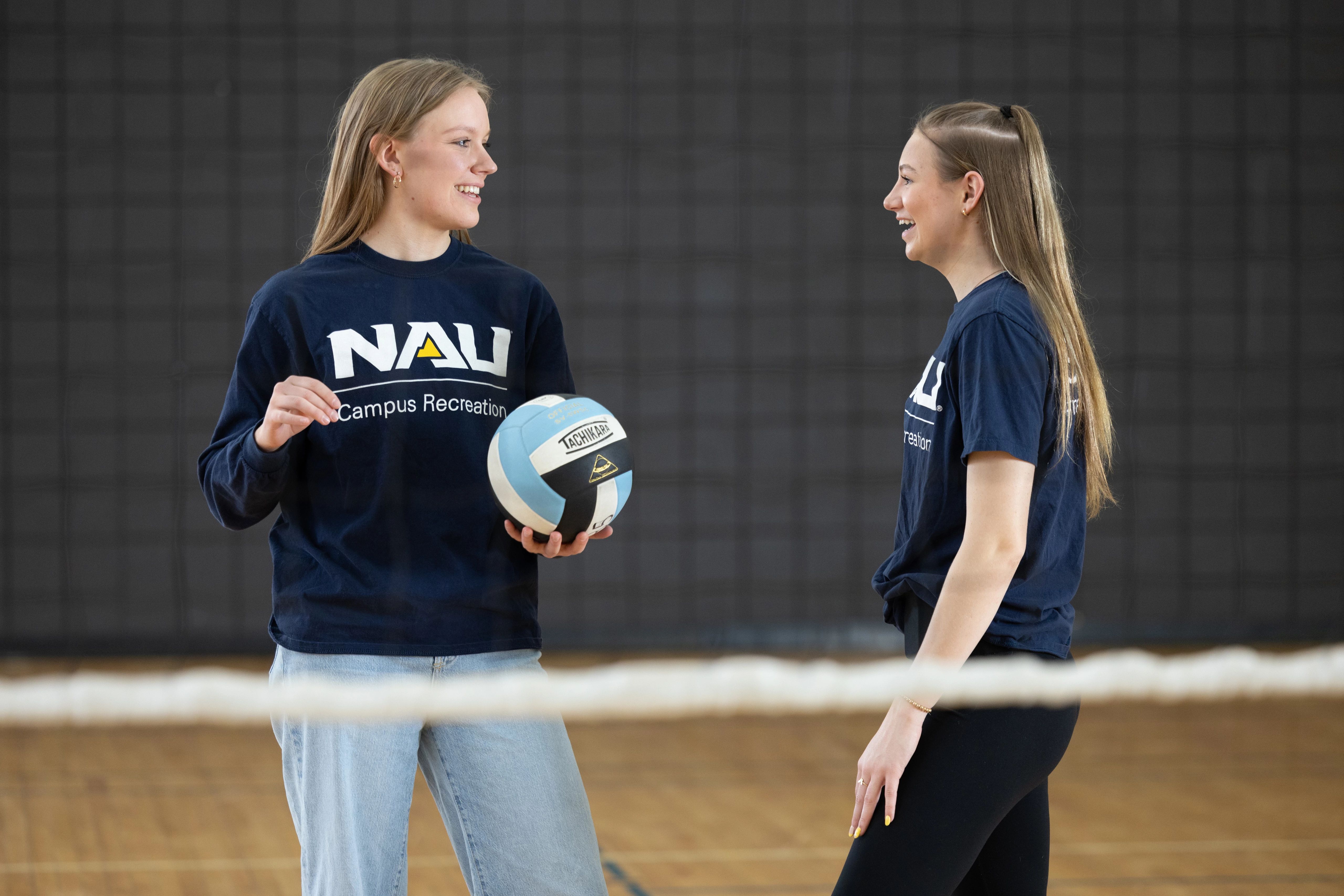 Students holding volleyball near net at campus recreation.