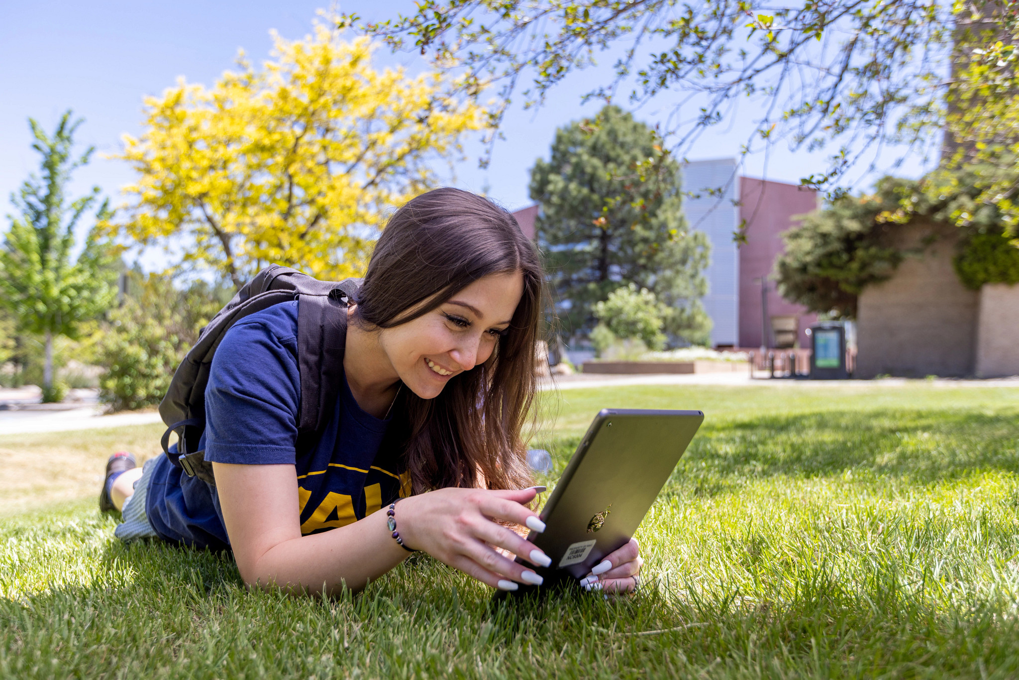 Smiling student Molly Garguilo reads tablet and lays on grassy lawn.