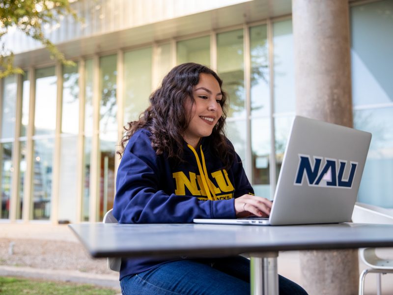 Student sitting outside at table working on a laptop.