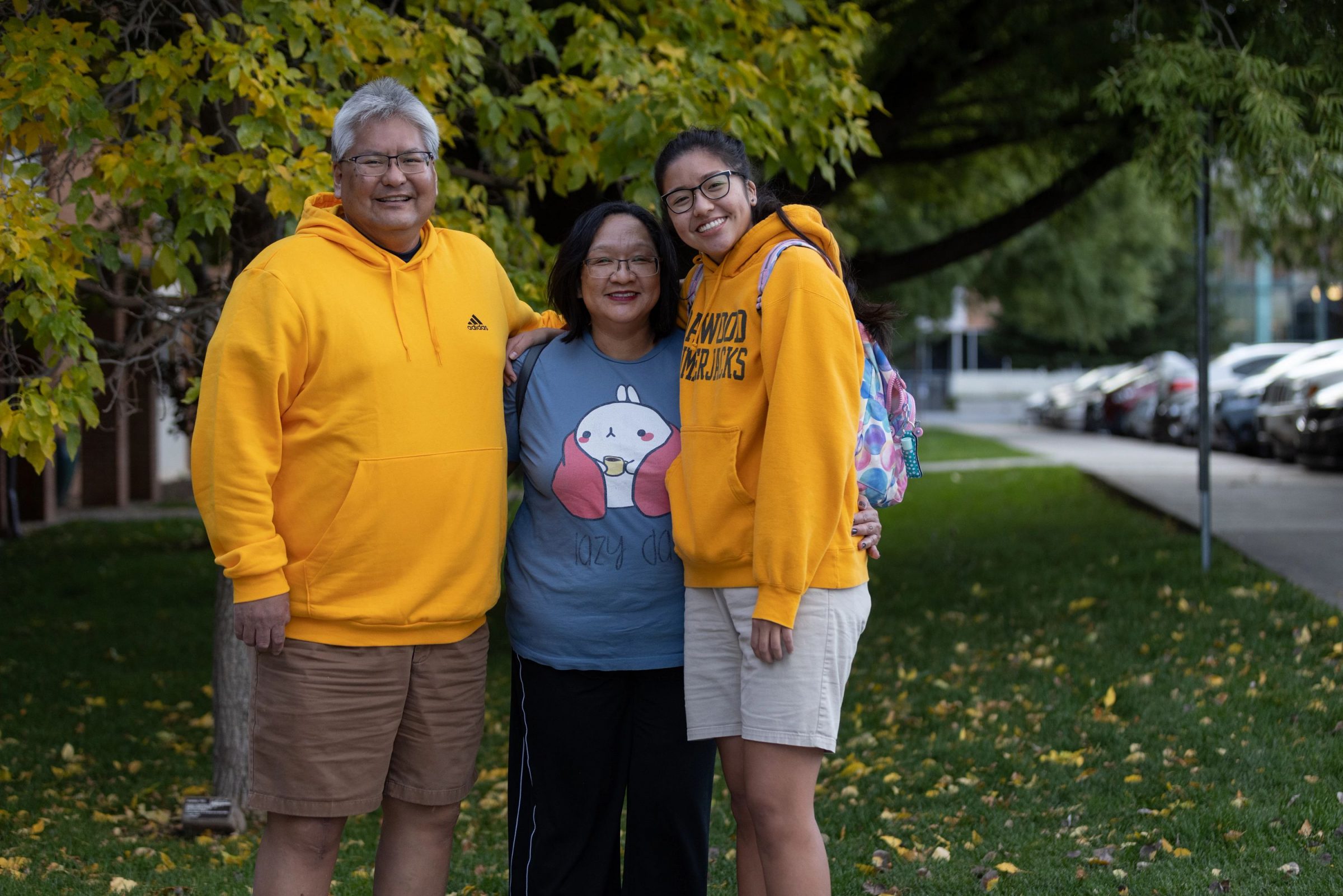 A family stands together smiling at the camera underneath a tree on campus.