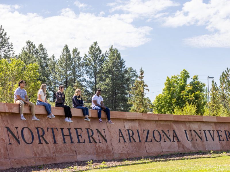 South N A U campus sign with students sitting on top of it.