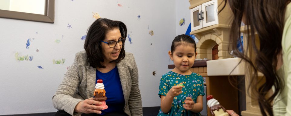A woman works with a young child playing with toys in the clinic. 