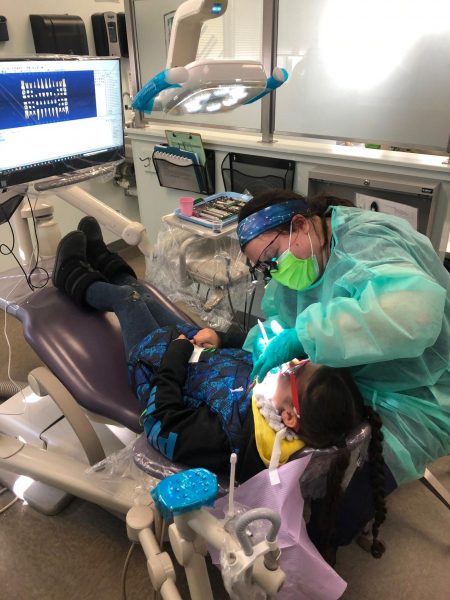A dental hygienist cleaning a kids teeth.