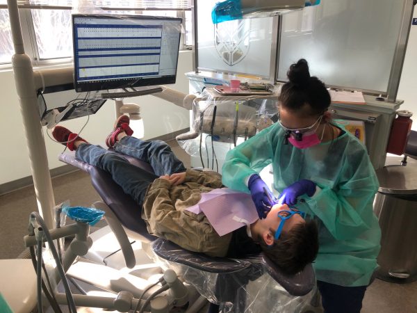A dental hygienist cleaning a kids teeth.