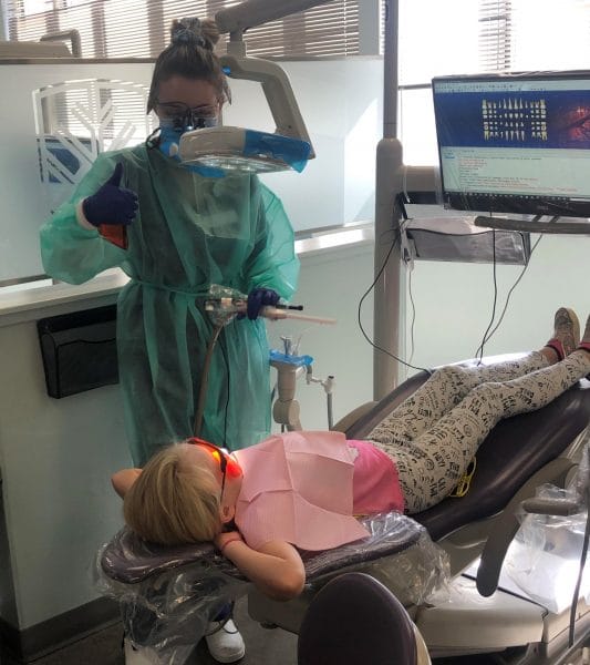 A dental hygienist cleaning a kids teeth.