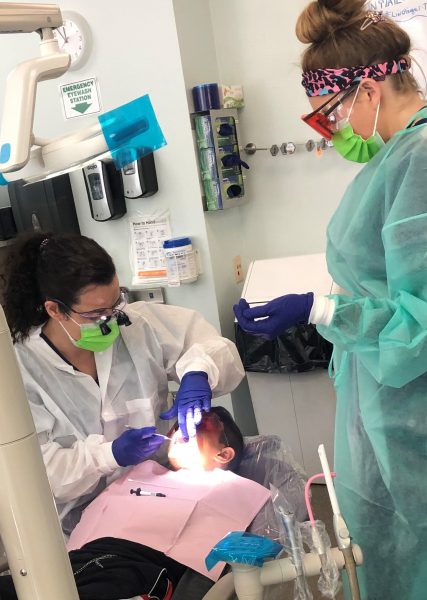 Two dental hygienists cleaning on a child's teeth.