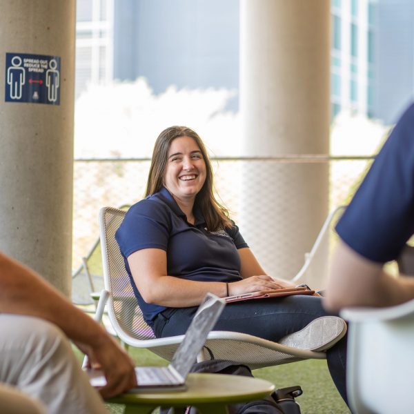 Click image to be directed to financial aid services. A seated brown haired female occupational therapy student smiles at peer nearby working on laptop. 