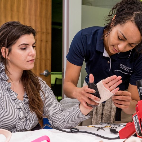 Click image to be directed to veteran and military services. Female occupational therapist adjusts and applies bandages and casting with tools on a female patient's hand while the patient watches. 