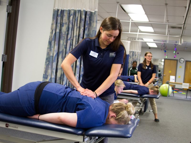 A physical therapy student rubs a patient’s back.